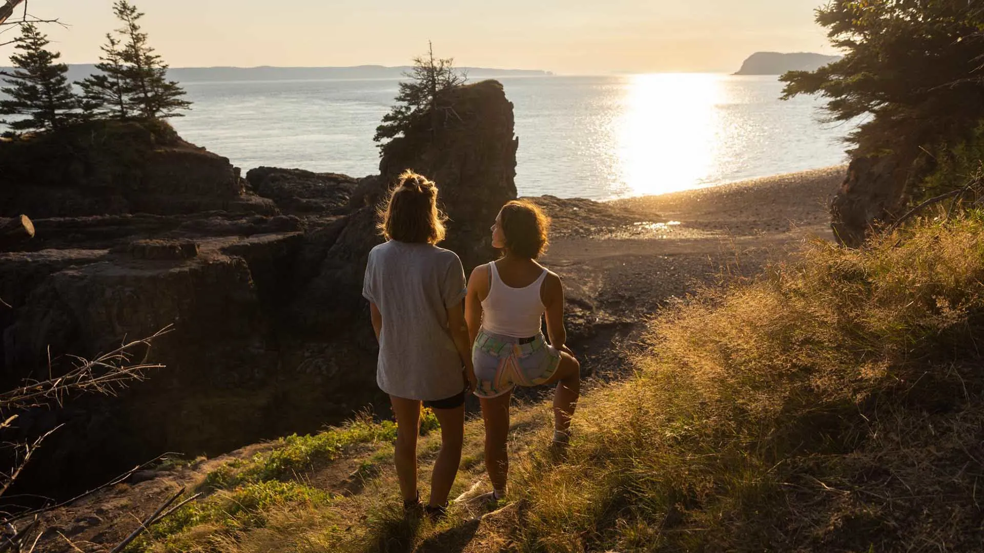 Two people hiking at Partridge Island within the Cliffs of Fundy UNESCO Global Geopark as the sun sets on the Bay of Fundy in Nova Scotia