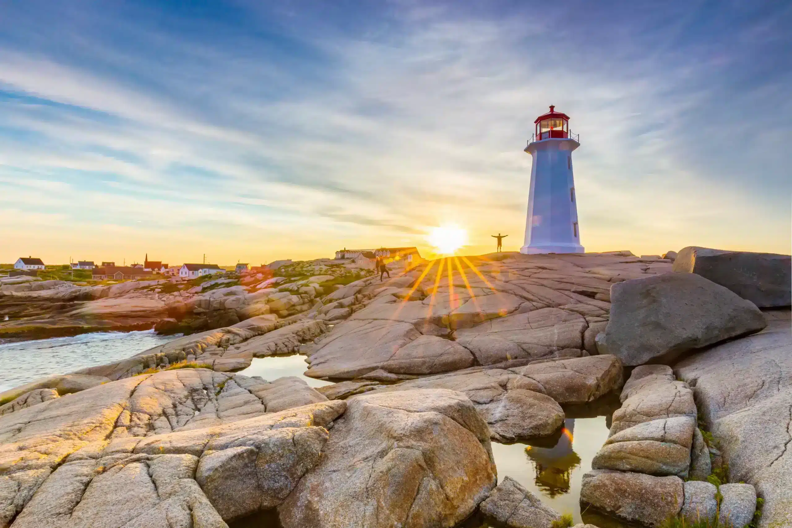 Peggy's Cove Lighthouse in summer at sunset with a person on the rocks