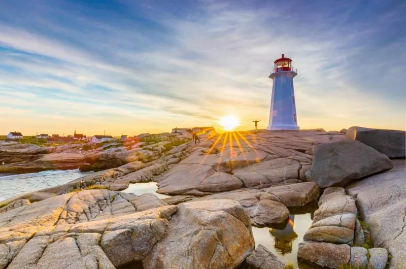 A person stands by Peggy's Cove Lighthouse on the rocks at sunset