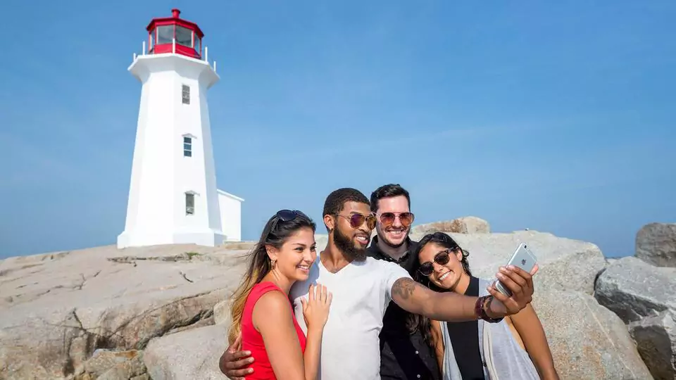 friends take selfie in front of peggy's cove lighthouse.