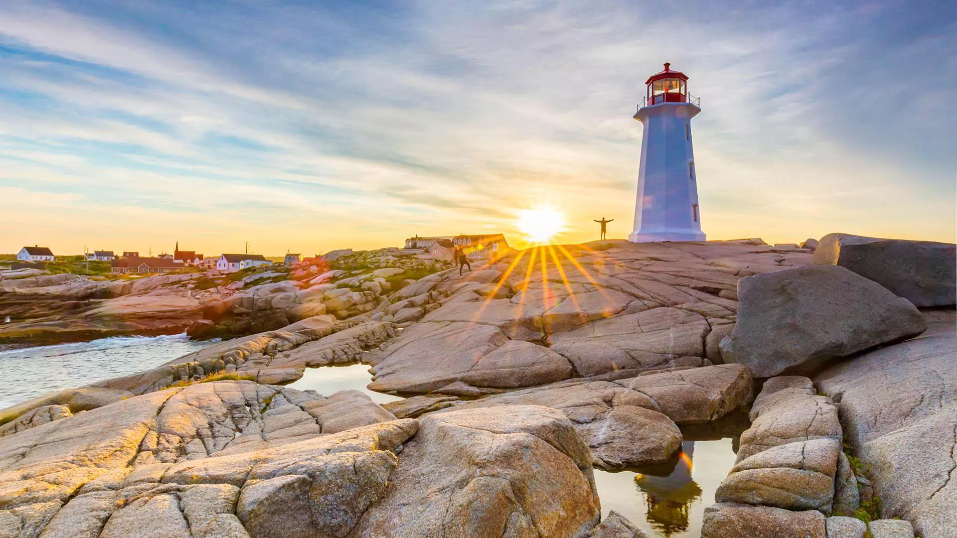 A person stands by Peggy's Cove Lighthouse on the rocks at sunset