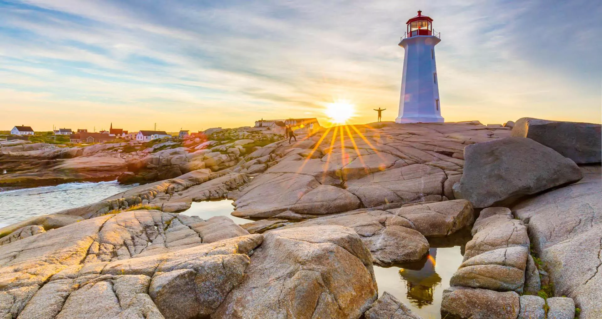 A person stands by Peggy's Cove Lighthouse on the rocks at sunset