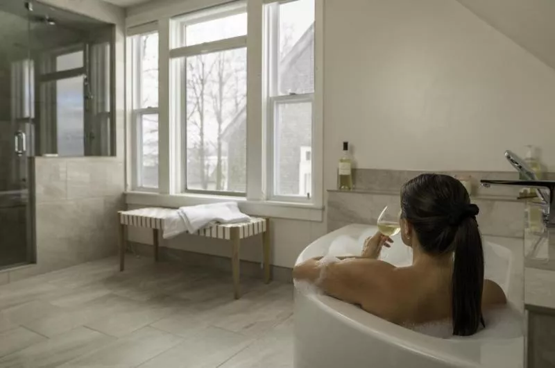 A person sits in a tub drinking a glass of wine inside one of the rooms at the Stay at Grand Pre Winery.