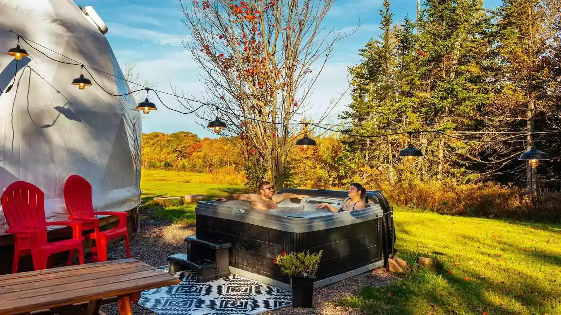 Two people relax in a hot tub next to a geo dome.